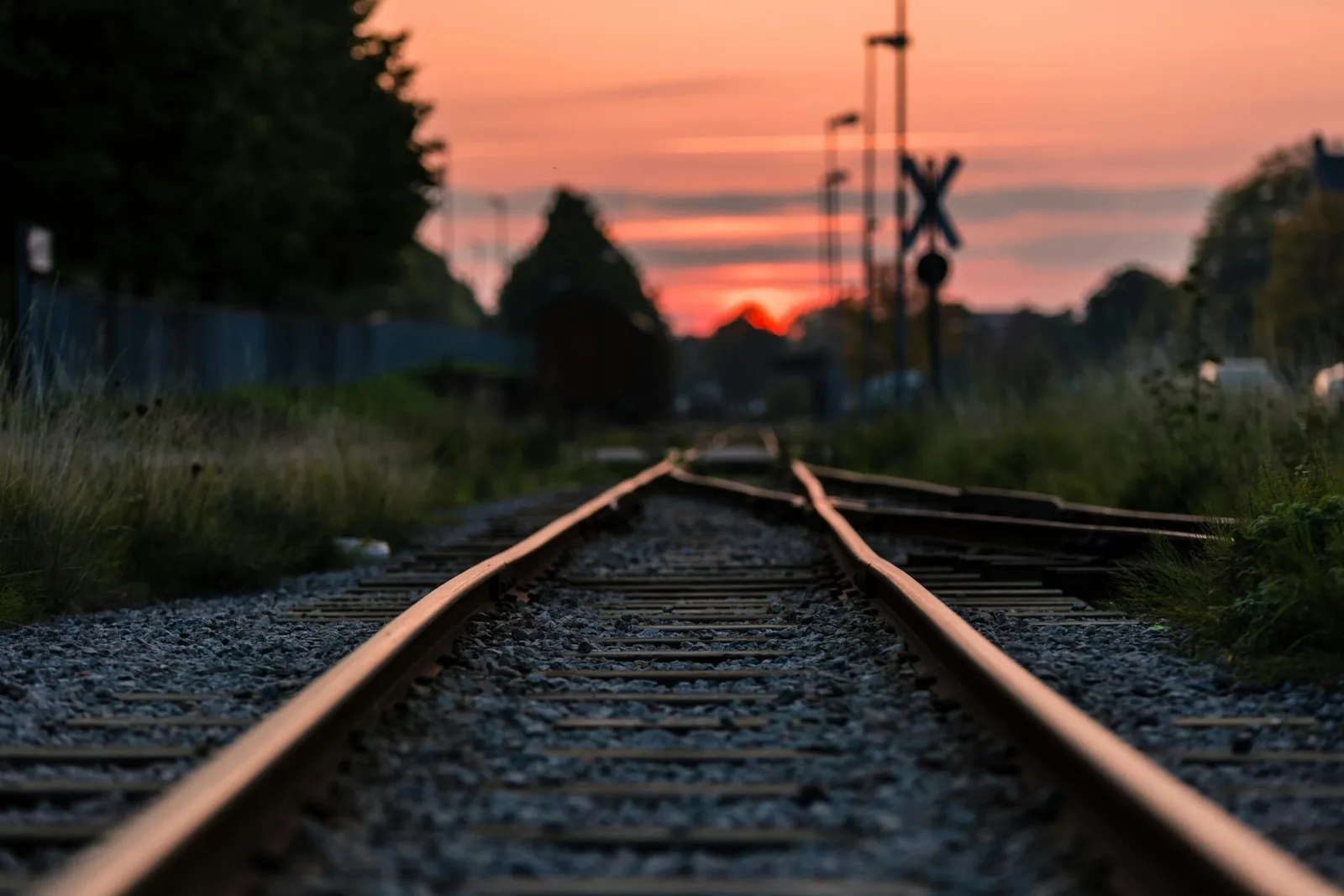 Uma ferrovia de trilhos de aço e dormentes de madeira ao pôr do sol, com um trem de carga distante e um sinal de cruzamento, representando o cenário para futuros projetos ferroviários brasileiros.