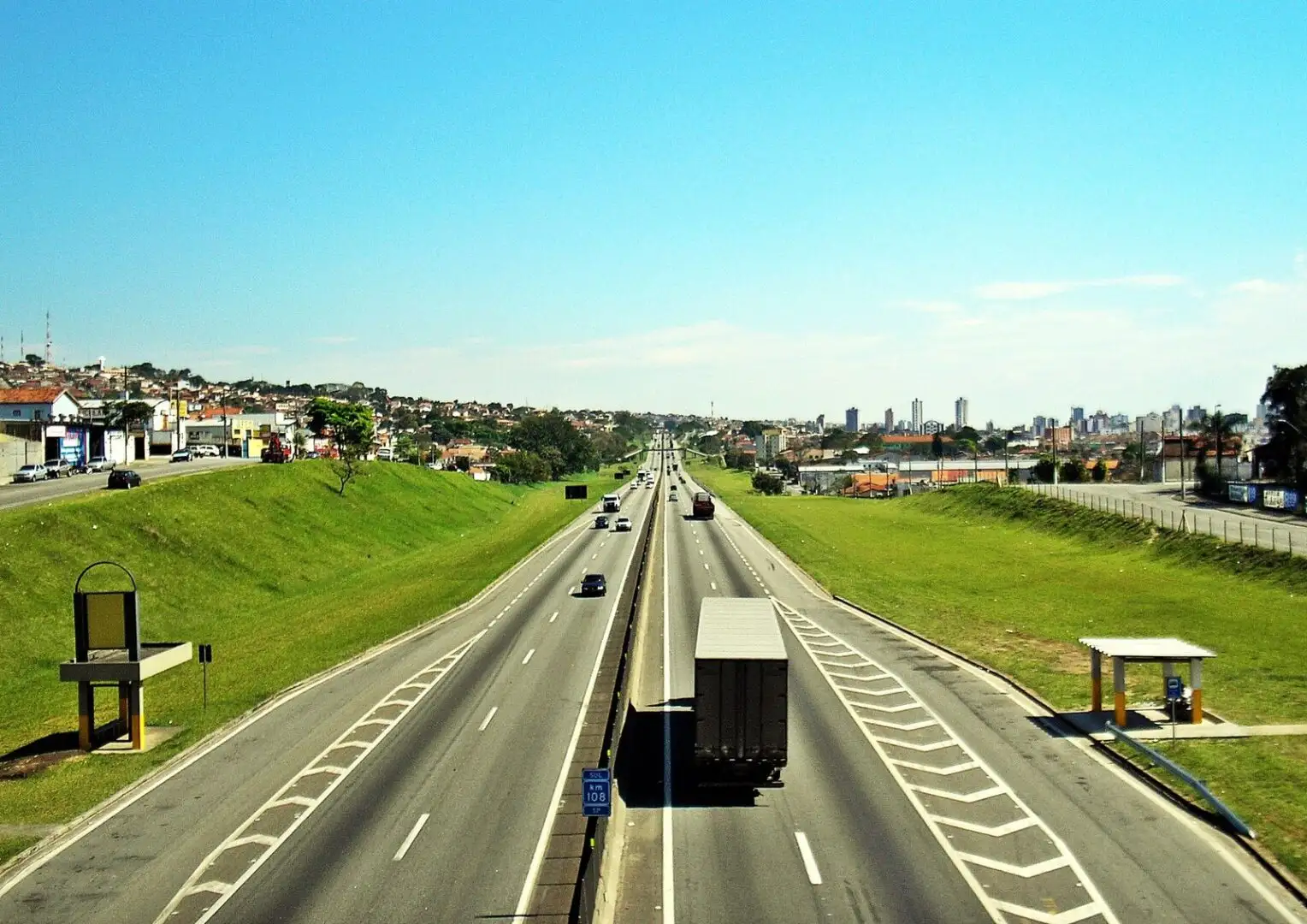 Vista panorâmica da Rodovia Presidente Dutra em Taubaté, com veículos e um caminhão de carga trafegando sob céu azul. Imagem de destaque sobre marketing de conteúdo para empresas de transportes.