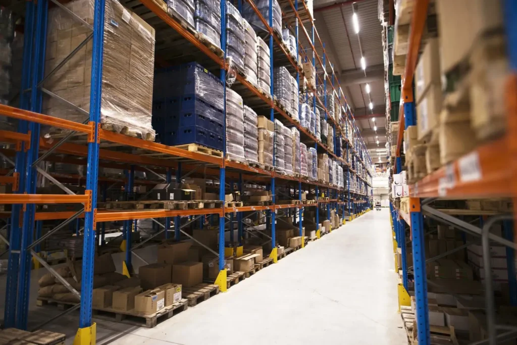 Interior de um amplo centro de distribuição logístico com altas prateleiras industriais repletas de caixas e produtos paletizados, setor fundamental nas estratégias de marketing para transporte e logística.