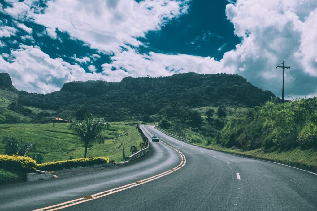 Uma estrada pitoresca serpenteando pelo campo, com montanhas ao fundo sob um céu azul.