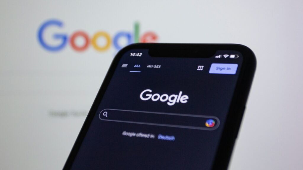 Smartphone exibindo a página inicial de busca do Google, com o logo da marca desfocado ao fundo