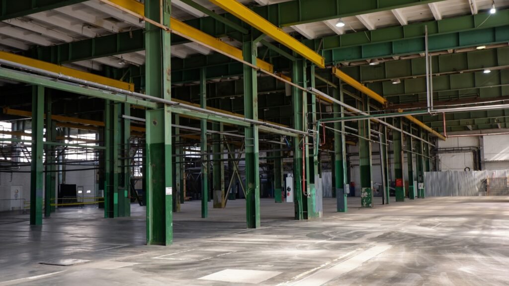 Interior vazio de galpão industrial com estrutura metálica verde e amarela e piso de concreto